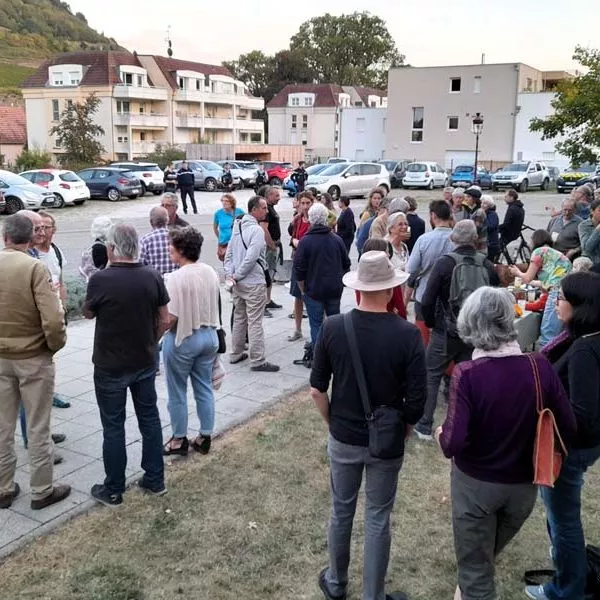 Plan large du rassemblement du 10 octobre 2023. Une cinquantaine de personnes discutent ou boivent de la soupe. En arrière-plan, au niveau du parking, il y a quatre gendarmes qui observent la scène.